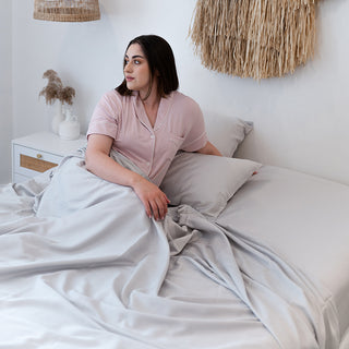 lady sitting under silver nimbus cloud bamboo sheets looking out the window with a pillow under arm