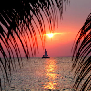 romantic blush orange sunset over the ocean with a small sailing boat in the distance