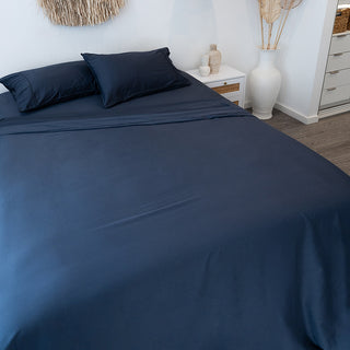 charcoal dark night bamboo sheets on bed with pillowcases in white wall room with white sideboard with wooden accessories