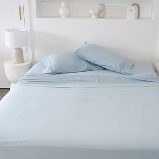 light ocean blue bamboo sheets with pillowcases in a white bedroom with a white stool with a white lamp shade