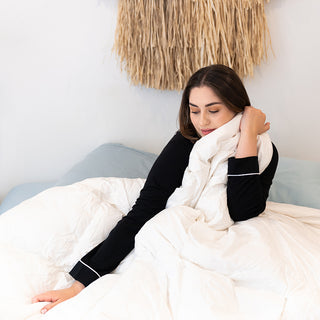  Relaxing woman on bed with pillows , enjoying the versatile 4 Seasons Goose Down Quilt for perfect sleep.