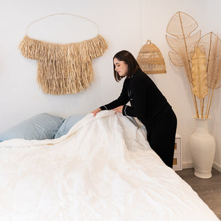A woman making a bed for a comfortable sleep on a bed with pillows and a tiki. Unlock the secret to ideal sleep with the 4 Seasons Goose Down