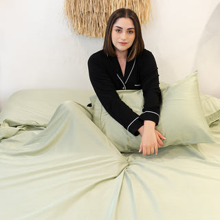 lady sitting on her bed under her green gum leaf bamboo sheets holding a pillow