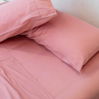 two pink sunset blush pillowcases on top of sheets on a made bed