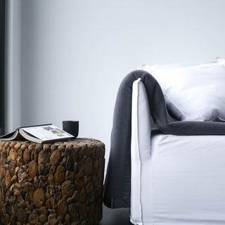 brown wooden stool on a white couch with a charcoal woolen blanket folded over couch arm