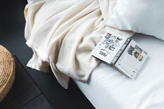 white couch with ivory woolen blanket with a book faced down open on the couch