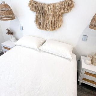 two white quilted pillow protectors on a white mattress protector in a white room with wooden furnishings