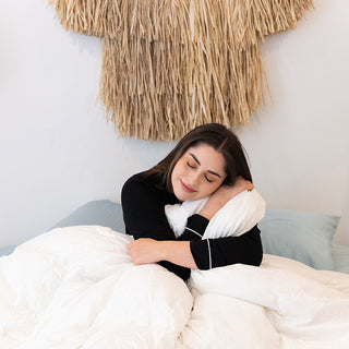 A woman enjoying a cozy night's sleep on a bed with pillows and a tiki, wrapped in the warmth of the Sienna Living Luxury Goose Feather Down Quilt.