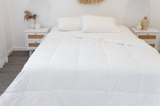 white bamboo quilt open on mattress on white sheets in a white room