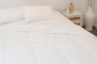 a close up shot of white bamboo quilt spread out on a mattress with white sheets
