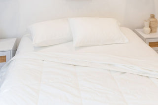 a white room with a white sheets and pillowcases with a white bamboo quilt on a mattress