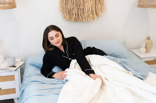 women lying in blue sheets with with her hand pulling back a bamboo quilt