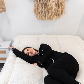 A woman in pajamas stretches on a bed, enjoying the comfort of a Sienna Living Snuggle mattress topper.